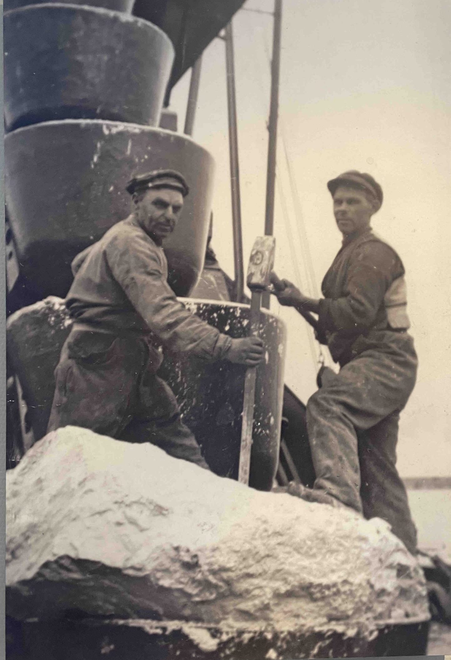 Manual labour to in the midst of a big machine. Two male workers and a chunk of harder sediment or rock on a bucket dredger. Photo by Henrik Ernstson of collections at Publikszentrum Water, Rotterdam, May 2022.